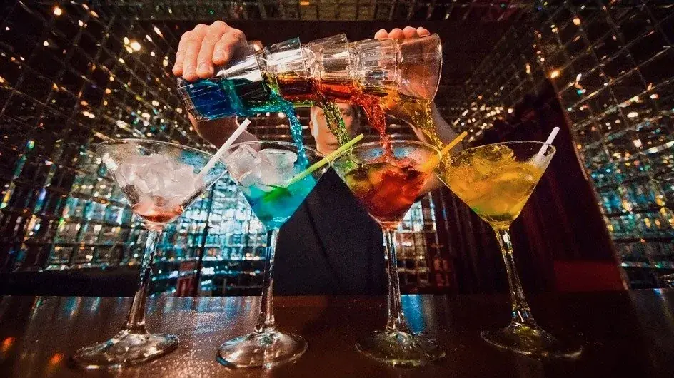 Bartender sirviendo una fila de cócteles de colores