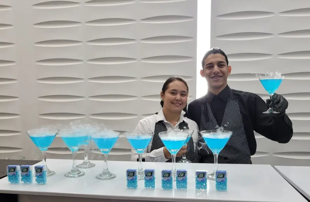 Dos bartenders junto a una mesa con cócteles azules listos para servir